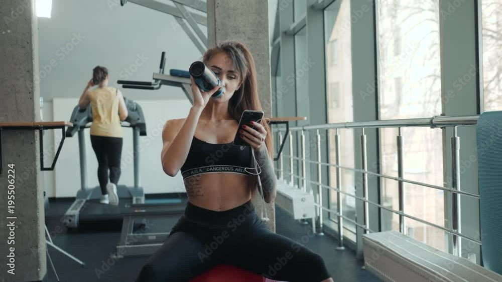 Young athletic woman drinking water in gym after hard workout . Young athletic woman drinking water in gym after hard workout .
