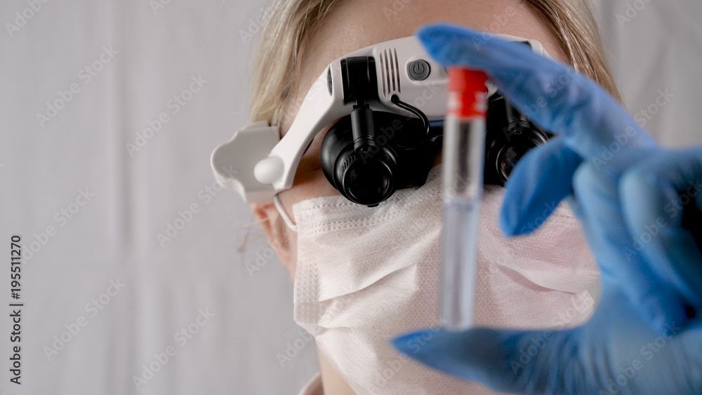 Laboratory work, a woman doctor holds a test tube, in a medical mask and professional glasses, a magnifying glass, takes an analysis from a test tube in blue rubber gloves, analysis, blood, DNA, a tes Laboratory work, a woman doctor holds a test tube, in a medical mask and professional glasses, a magnifying glass, takes an analysis from a test tube in blue rubber gloves, analysis, blood, DNA, a tes
