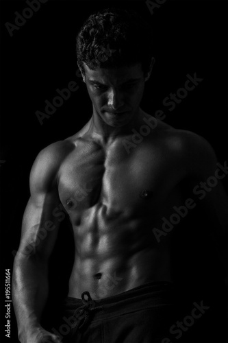 Highly retouched black and white fitness model and bodybuilder, Looking and posing abs and chest. concept of power, strength and self-confidence. black background.