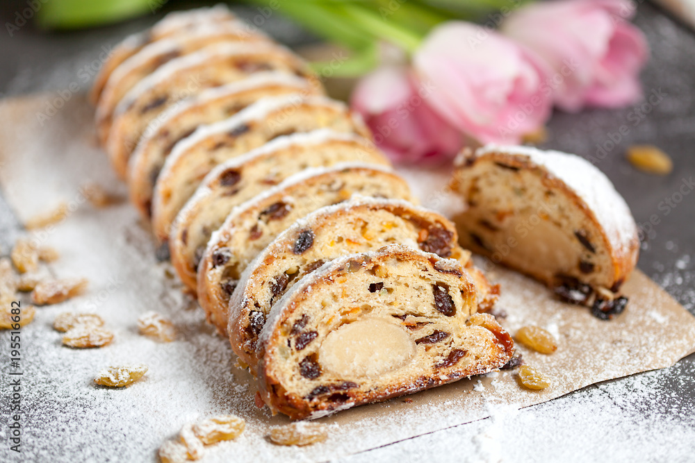 freshly baked cake with sweets, raisins and candied fruits, sprinkled with powdered sugar on a gray table with pink tulips