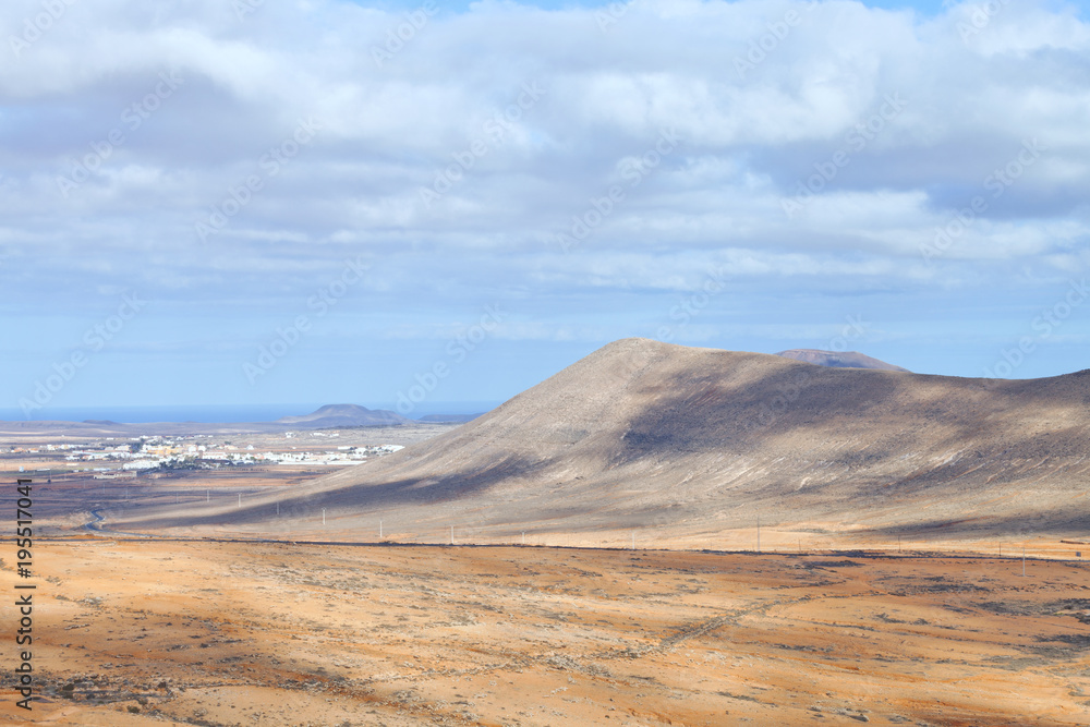 Aerial view of arid desert valley with volcano peaks, coast village, on a summer, cloudy day, Fuerteventura, Canary Islands, Spain .