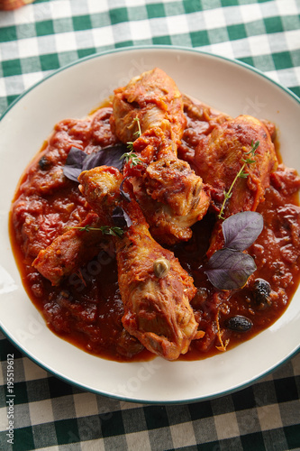 Chicken legs cooked in italian cacciatore style with tomato sauce and fresh basil on green checkered table-cloth