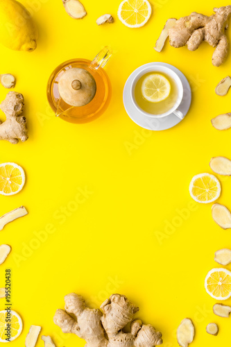 Warming tea with lemon and ginger. Cup, teapot, ginger root on yellow background top view copy space