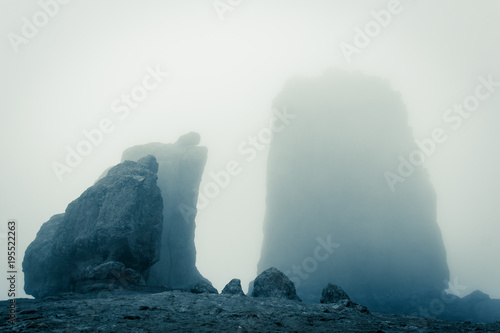 Fototapeta Naklejka Na Ścianę i Meble -  Roque Nublo big rock mountain covered with heavy fog in Gran Canaria, Spain. Futuristic sci fi landscape setting. Thriller, mysterious empty space. Blue effect