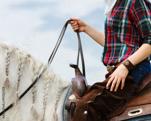 The cowboy on a white horse in western style holds the reins on a blue sky background isolated. Detail closeup photo