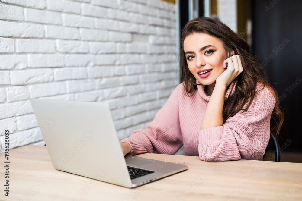 Happy casual beautiful woman working on a laptop sitting at table in the house. Happy casual beautiful woman working on a laptop sitting at table in the house.