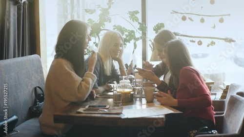 Smiling Girl showing something on a smartphone to friends while sitting in a cafe