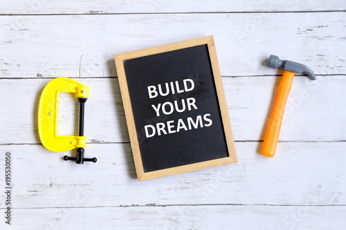 Top view of clamp,hammer and blackboard written with ' BUILD YOUR DREAMS' on white wooden background. photo