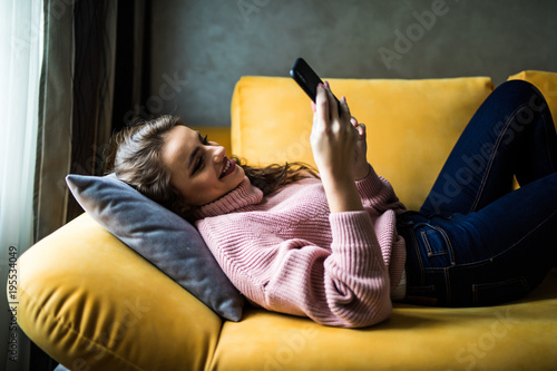 Close up of a relaxed girl using a smart phone lying on a sofa in the living room at home photo