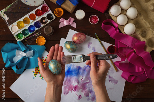 Happy Easter. Women's hands in time Painting Easter eggs on a background of a dark wooden table