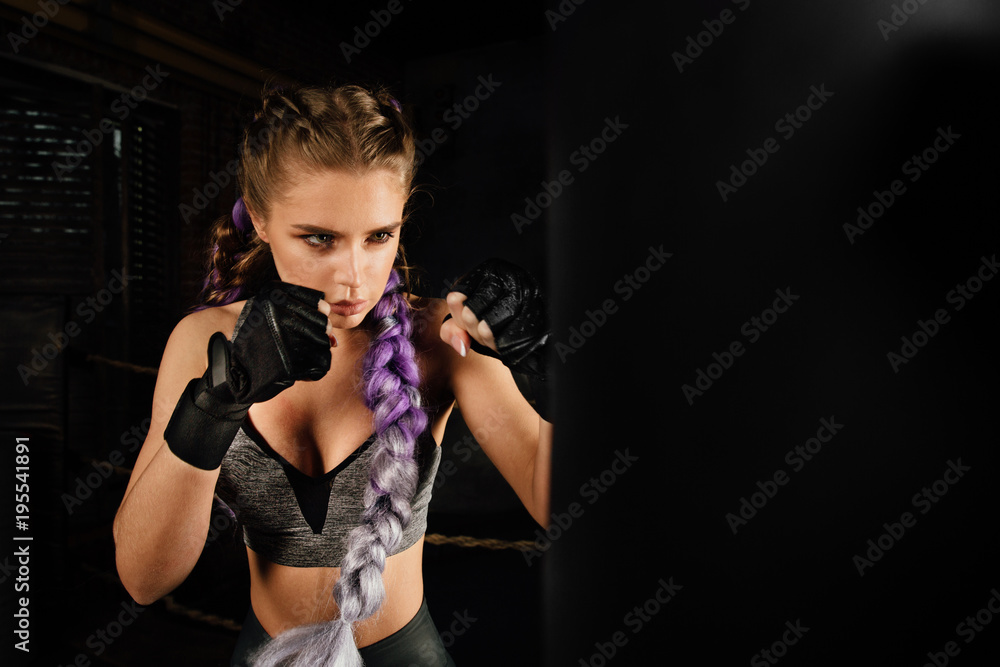 Young woman trains in boxing ring with heavy punching bag.