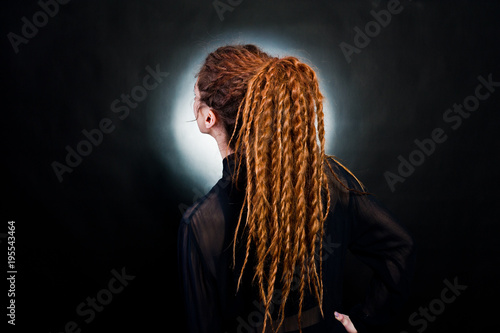 Studio shoot back of girl in black with dreads at black background with nimbus.