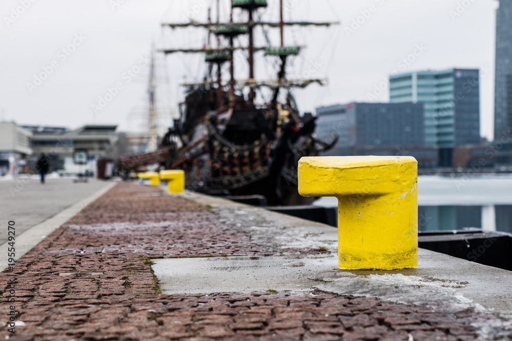 A mooring bollard entwined with a mooring rope. Moored ships at the port quay. A mooring bollard entwined with a mooring rope. Moored ships at the port quay.