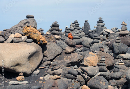 beautiful towers of stacked pebbles and stones in a large arrangement on a black sand beach with blue sky