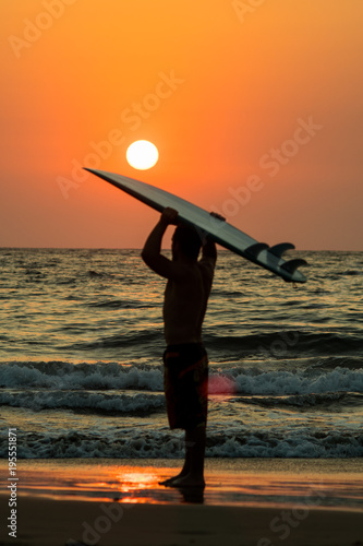 surfer walking on beach at sunset