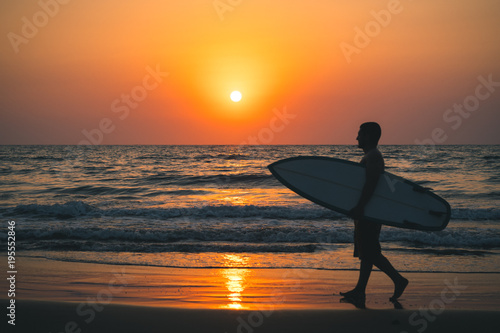 surfer walking on beach at sunset