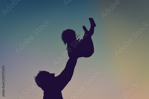 Silhouette of happy family, joyful father throwing up his child in the park on the sunset sky outdoors background