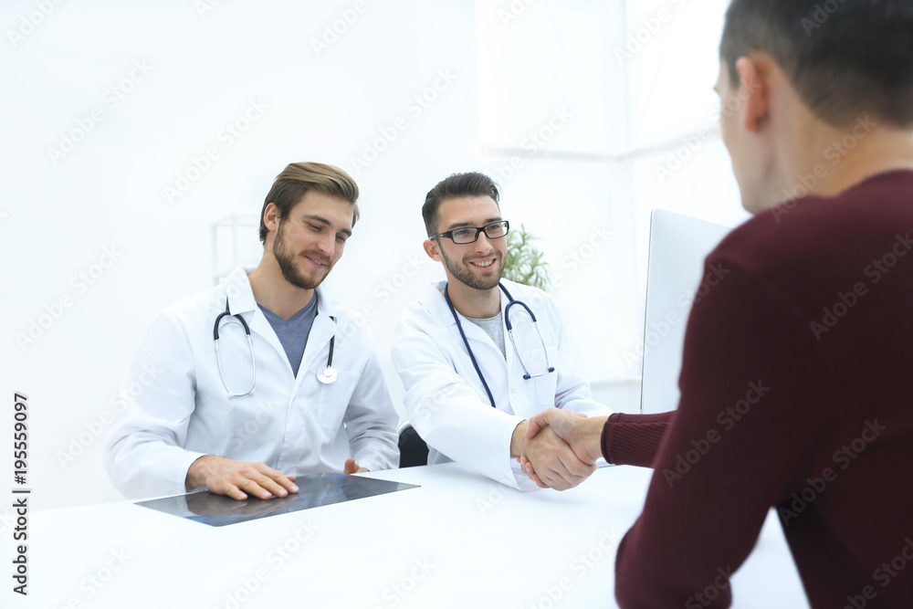 Smiling doctor at the clinic giving an handshake to his patient