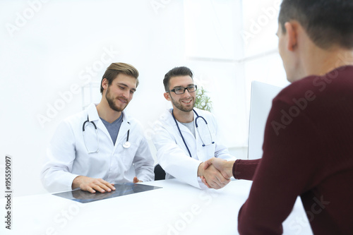 Smiling doctor at the clinic giving an handshake to his patient