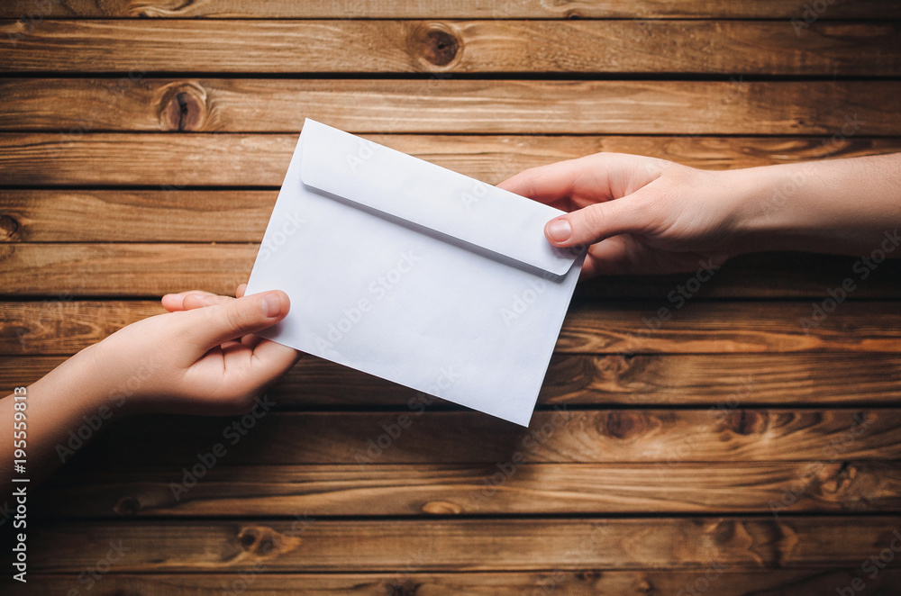 One hand passes a white envelope to the other hand on a wooden background. Transfer of money for donation. One hand passes a white envelope to the other hand on a wooden background. Transfer of money for donation.