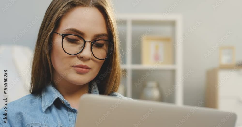 Portrait shot of the serious young woman in glasses working on the laptop computer at home in the living room. Close up Portrait shot of the serious young woman in glasses working on the laptop computer at home in the living room. Close up