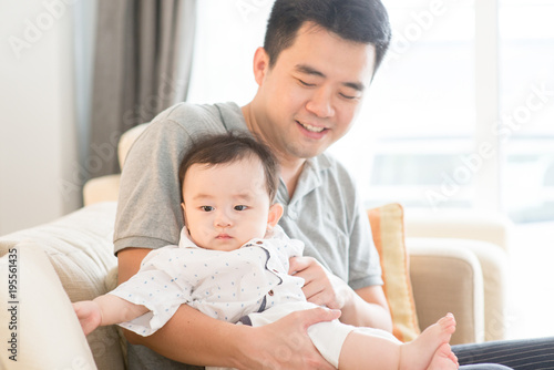 Father holding baby sitting on sofa.