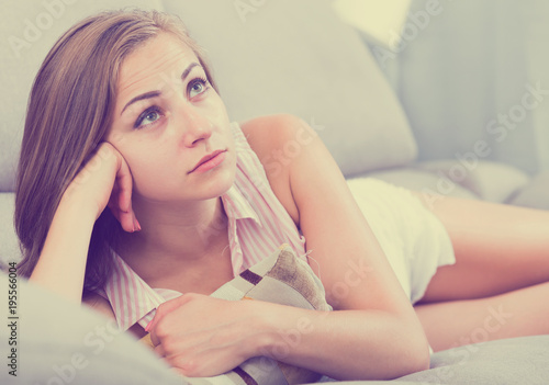 Disappointed girl lying on couch with cushion