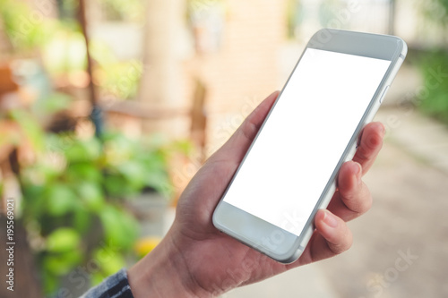 Mockup image of a hand holding and showing white smart phone with blank desktop screen in outdoor with blur green nature background