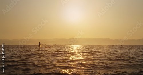 Fototapeta Naklejka Na Ścianę i Meble -  Fisher with a cap on a boat in a Myanmar water body in a sunset
