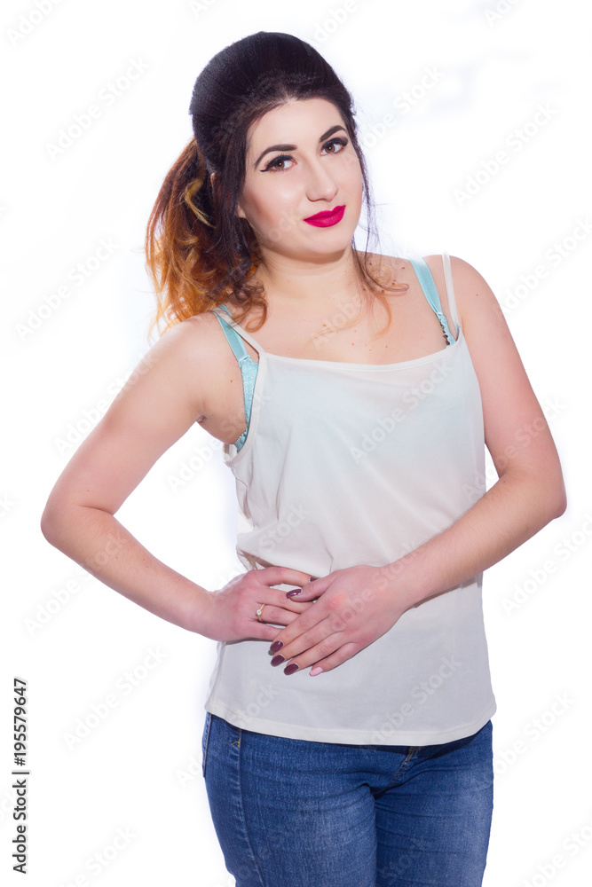 Obraz premium Studio portrait of a beautiful young woman with black hair gathered in a tail. A girl in a T-shirt and jeans poses against a white background. He looks at the camera. Isolate