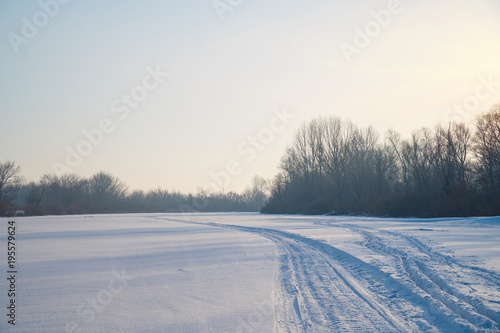Trees in the frosty air on a snow-covered glade. Winter landscape. On the snow you can see the track from the snowmobile
