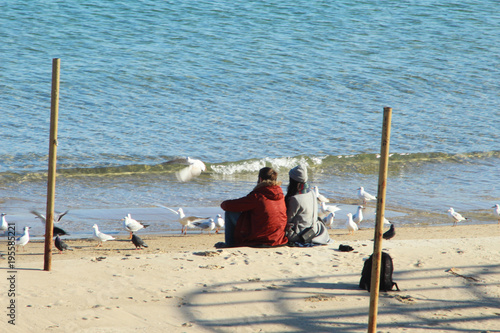 a young man and a girl are sitting on a sandy beach near the sea