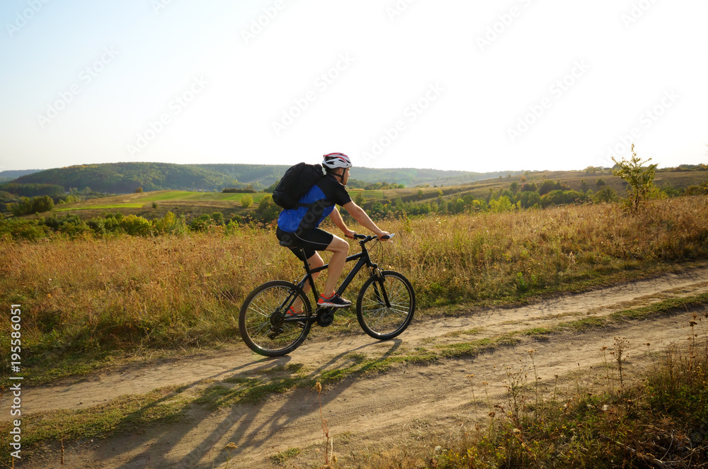 Male cyclist with backpack driving by rural dirt road outdoors Male cyclist with backpack driving by rural dirt road outdoors
