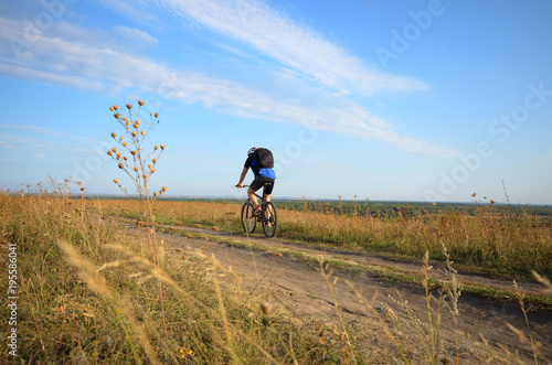 Male cyclist with backpack driving by rural dirt road outdoors © Mikhailov Studio