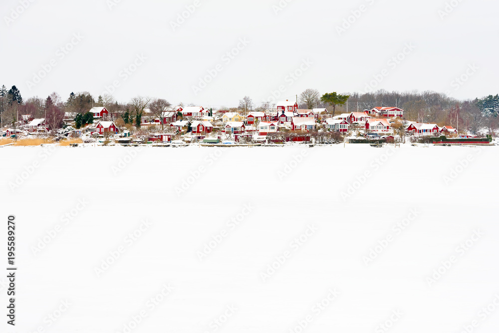Brandaholm (Karlskrona, Sweden) allotment village with small red cabins in winter landscape. Frozen sea covered in snow in the foreground.