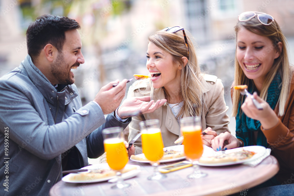 Group of three friends using phone in outdoor cafe on sunny day, eating pizza Group of three friends using phone in outdoor cafe on sunny day, eating pizza