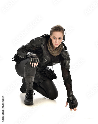 full length portrait of female soldier wearing black tactical armour, seated pose, isolated on white studio background.