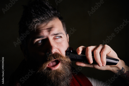 Canvas Print Portrait of brutal man shaving his face, his beard with electric razor while