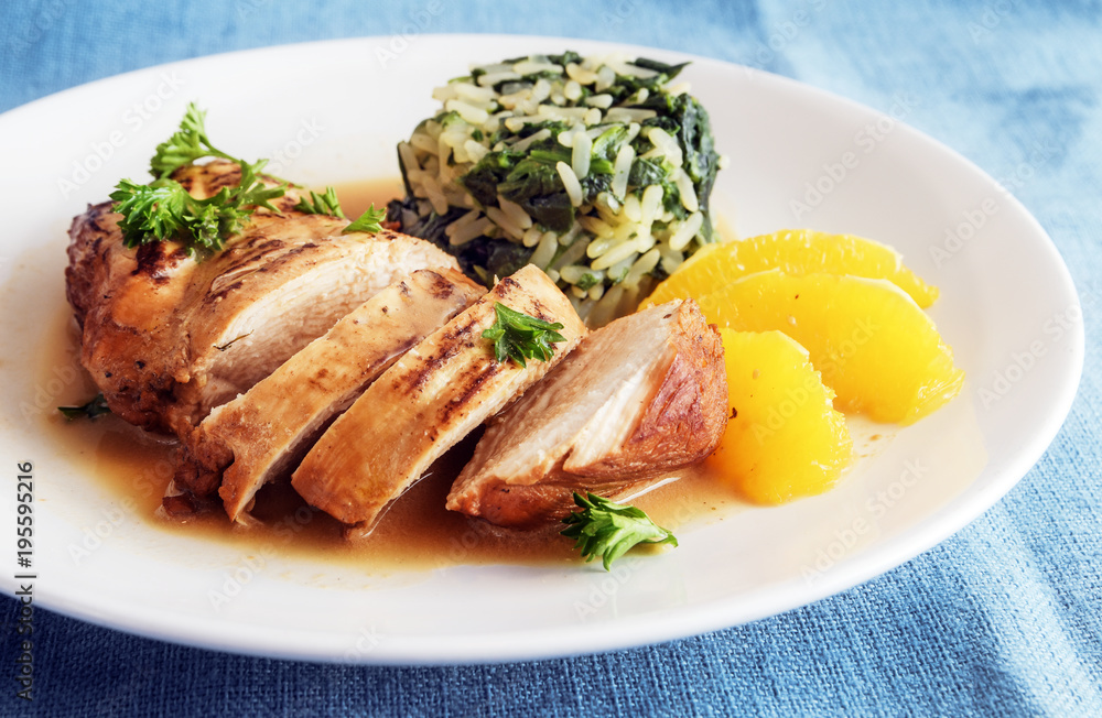 Chicken breast with orange slices and spinach rice on a white plate, diet dinner with low calories, blue tablecloth Chicken breast with orange slices and spinach rice on a white plate, diet dinner with low calories, blue tablecloth