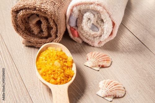 Wooden spoon with yellow sea salt for bathroom procedures with towels on the background