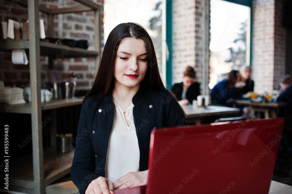 Fototapeta premium Brunette girl sitting on cafe and working with red laptop.