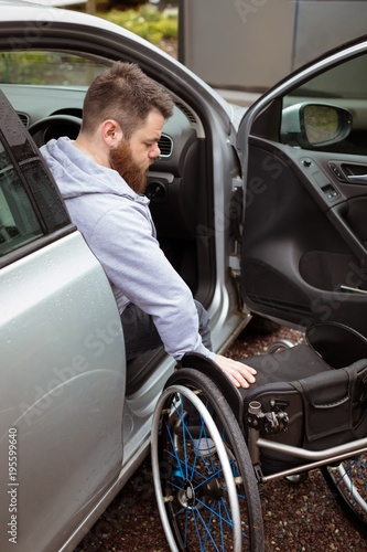 Disabled man holding wheelchair while boarding in his car photo