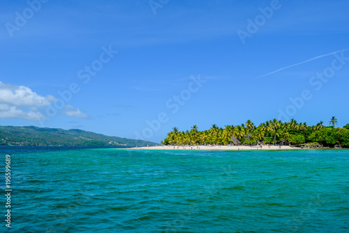 Beautiful beach with palms, blue sky and turquoise water, some tourists having fun, relaxing and swimming in the ocean, caribbean sea