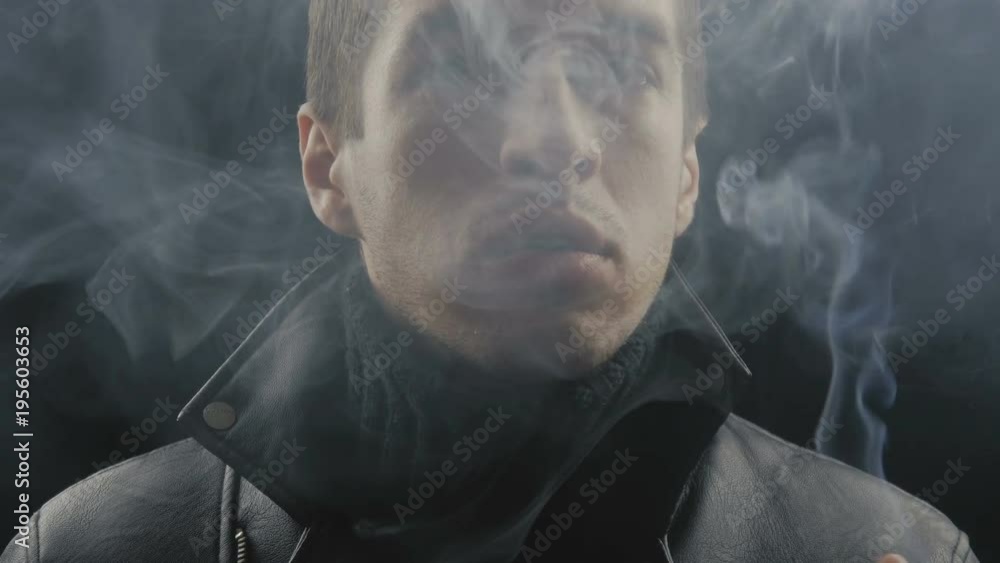 close-up of young man smokes cigarettes at black background