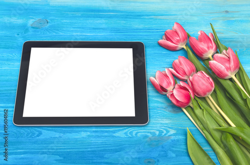 Fototapeta Naklejka Na Ścianę i Meble -  Tulip flowers and tablet computer device with blank screen on blue wooden table board background with copy space. Woman day concept. Mother day background. Saint Valentines day greeting card mock up. 