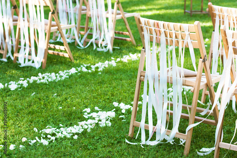 Wooden chairs decorated with bows and path of petals on wedding ceremony outdoors Wooden chairs decorated with bows and path of petals on wedding ceremony outdoors