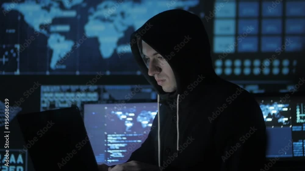 Man geek hacker in hood working at computer in cyber security center filled with display screens. Man geek hacker in hood working at computer in cyber security center filled with display screens.
