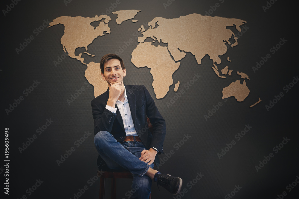 Young man looking to world map with crossed hands Young man looking to world map with crossed hands