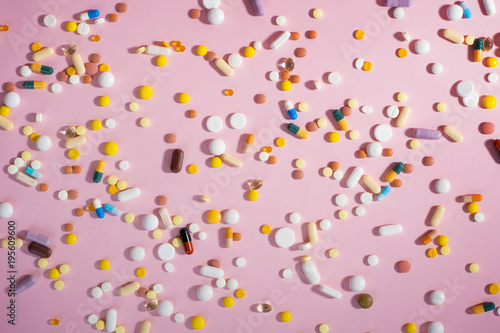 Background with medicines, pills, supplements and vitamins tablets on pink background.