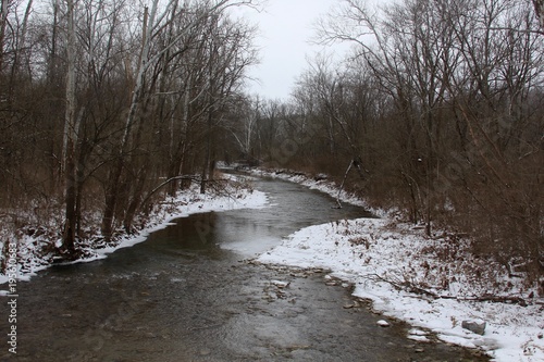 The flowing creek in the winter uno covered forest. 